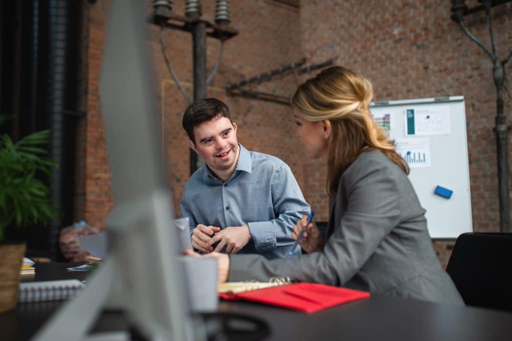 Happy down syndrome man with businesswoman colleague working in office, social inclusion and cooperation concept.